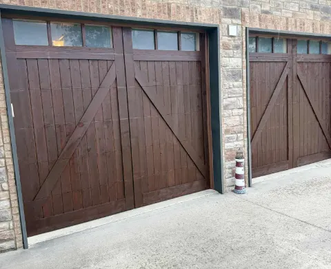 Carriage-style garage doors refinished in a dark wood stain on a brick and stone house