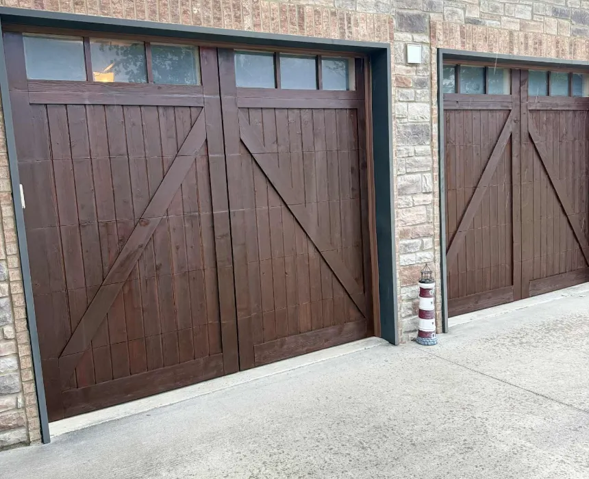 Carriage-style garage doors refinished in a dark wood stain on a brick and stone house